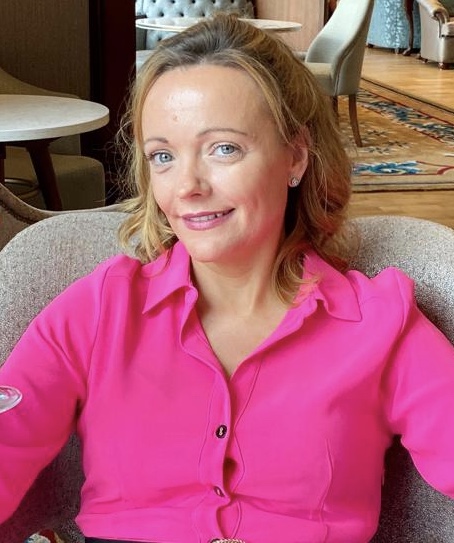 Fiona, a blonde lady in a pink blouse sitting in a chair