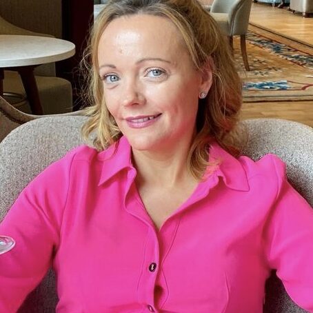 Fiona, a blonde lady in a pink blouse sitting in a chair